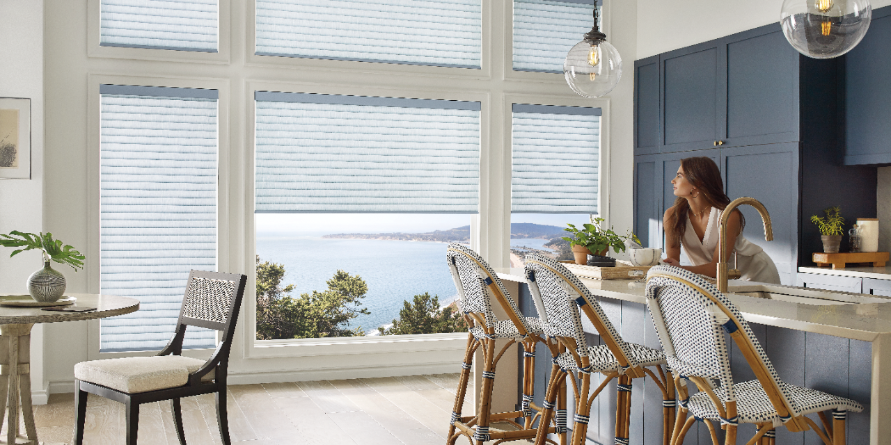 A woman in a kitchen gazing out large picture windows with Sonnette PowerView Shades.